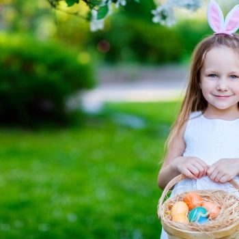 a young girl with easter bunny ears on and holding a basket.