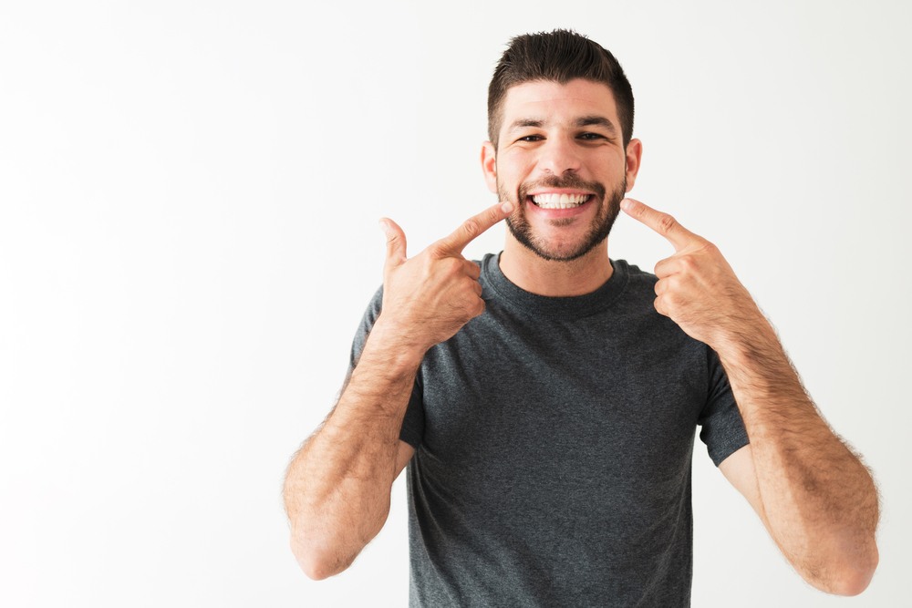 A man pointing to the results of his dental bonding procedure. His teeth are white and bright.